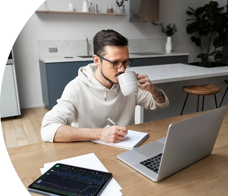 Trader analyzing charts on a tablet and working on a laptop